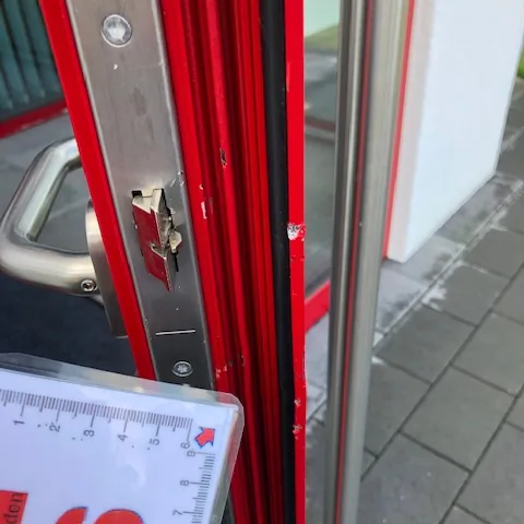 Aus dem Rahmen gehebeltes Schließblech einer roten Aluminium-Tür